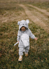Little child in a plush mouse costume walking in an open field.