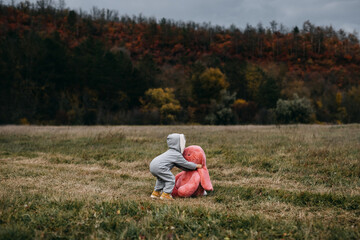 Little child wearing a bunny costume, playing with a big pink plush bunny toy, outdoors, in an open field.