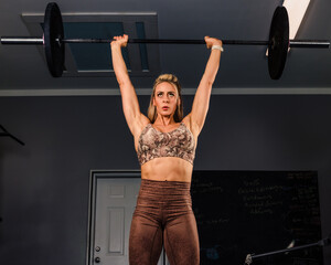 Woman doing overhead press with barbell. 