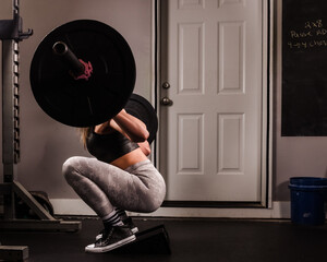 Woman doing a squat with barbell at a home gym.