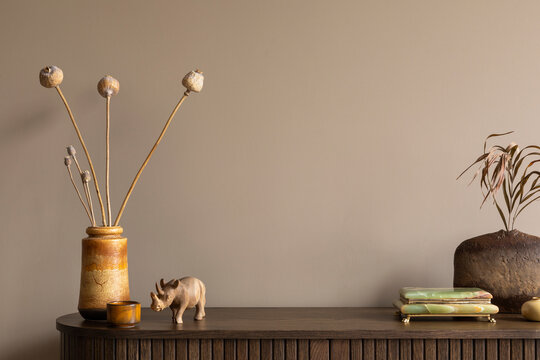 Creative composition of living room interior with wooden sideboard, stylish vase with dried flowers, stylish casket, nuts in bowl, brown wall and personal accessories. Home decor. Template.