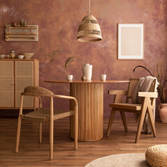 Stylish boho vintage dining room interior with poster mock up. Round table with rattan armchair, round carpet with pouf, vase with dried flowers and cup. Brown wall and rattan lamp.