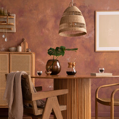 Stylish boho vintage dining room interior with poster mock up. Round table with rattan chair, vase with dried flowers. Brown wall and rattan lamp. Mock up poster. Template.