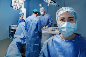 Fototapeta na wymiar Operating theatre nurse. Portrait of surgical nurse wearing medical scrub and protective face mask over background operation room with surgery staff