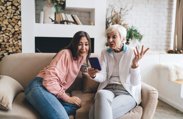 Obraz premium Confused senior diverse women surfing internet on smartphone