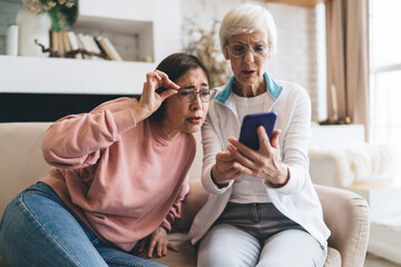 Elderly diverse girlfriends squinting while browsing smartphone