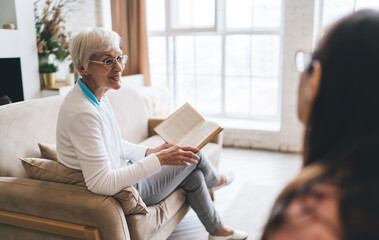 Senior woman reading book while sitting on sofa in living room