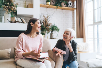 Joyful diverse women with gift box sitting in living room
