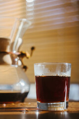 Black coffee in a glass cup with kemex on a sunny wooden table.