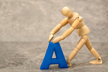A wooden mannequin holding a plastic letter A