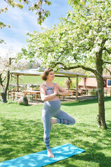 Outdoor portrait of happy young pregnant woman practicing youga in spring garden under blooming apple trees, healthy lifestyle