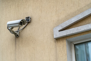Dirty outdoor surveillance camera mounted on beige plaster wall. CCTV security camera outdoors.