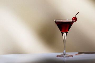 Black Manhattan cocktail with whiskey and red vermouth garnished with maraschino cocktail cherry in martini glass. Beige background, hard light