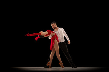 Beautiful, talented, attractive young man and woman, professional dancers performing, dancing tango over black background. Concept of lifestyle, action, beauty of movements, emotions, fashion, art