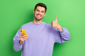 Photo of handsome guy toothy smile hold telephone show thumb up feedback isolated on green color background