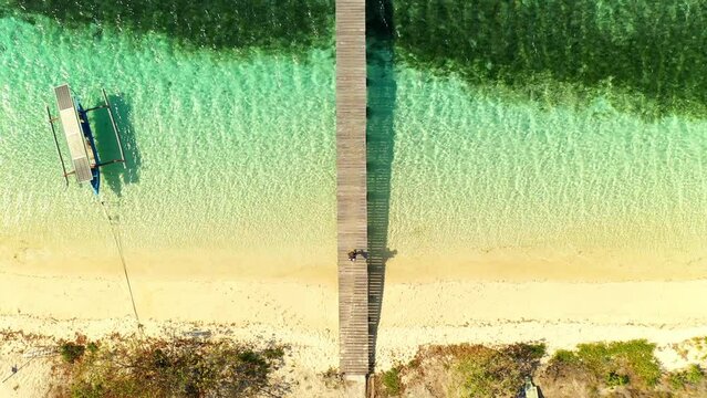 Aerial Top Forward Shot Of Person Walking On Jetty Towards Outriggers Over Turquoise Sea During Sunny Day - Lombok, Indonesia