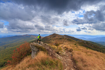 Fototapeta premium female tourist in a green jacket on a rock in the mountains