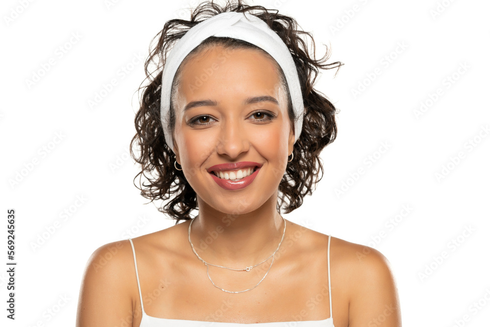 Wall mural Young dark skinned smiling woman with makeup and headband posing on a white background