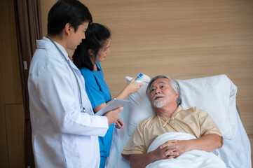 Obraz premium Smiling senior male patient lying and sitting on bed resting while nurse and doctor in lab coat and stethoscope showing digital tablet screen to man in a hospital room