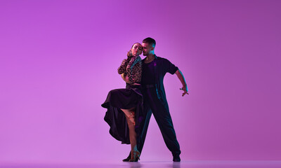 Passion. Man and woman, professional dancers in stylish, beautiful stage costumes performing tango over purple background on neon lights. Concept of hobby, lifestyle, action, emotions, fashion, art - obrazy, fototapety, plakaty
