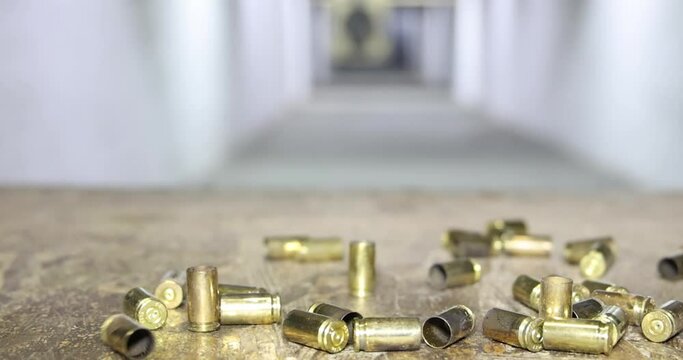 Empty bullet shells fall down after firing in indoor shooting range, slow motion. Gun shooting at a target, close up