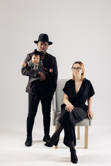 Happy interracial family with baby daughter poses near armchair against white background.