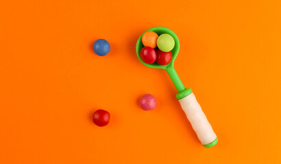 Round multi-colored candies in a green baby spoon on an orange background