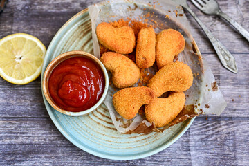 
 Crispy oven baked  chicken nuggets and ketchup. Breaded chicken fillets  with chilly peppers and fresh basi on wooden rustic background