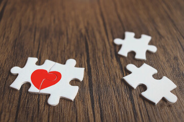Two pieces of puzzle forming red heart on brown wooden, heart on pieces of jigsaw, romantic background for celebrating anniversary on Valentine day, love unity of a couple in love couple.