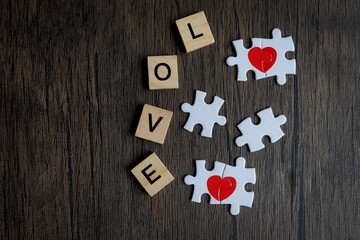 Text wooden blocks spelling the word LOVE and puzzle forming red heart  brown wooden, romantic background for celebrating anniversary on Valentine day, love unity of a couple