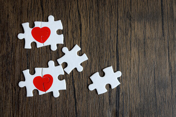 Two pieces of puzzle forming red heart on  brown wooden, heart on pieces of jigsaw, romantic background for celebrating anniversary on Valentine day, love unity of a couple 
