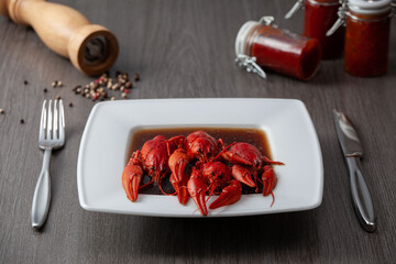 Portion of boiled crawfish on a square plate with pepper on the table