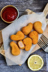 
 Crispy oven baked  chicken nuggets and ketchup. Breaded chicken fillets  with chilly peppers and fresh basi on wooden rustic background