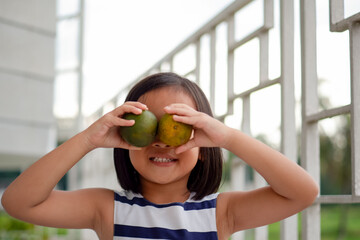 cute little asian child holding two orange fruit in front of her eyes