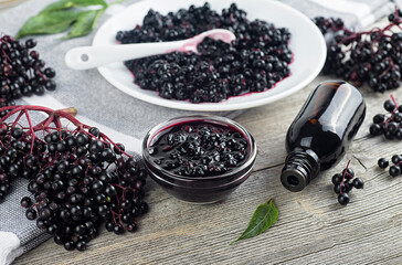 Homemade black elderberry syrup in ceramic jar and bunches of black elderberry with green leaves on...
