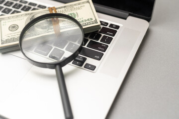 Magnifying glass and dollar bills on laptop. Search for financial income on Internet.