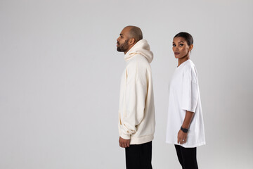An african american man in a white hoodie and a woman in a white t-shirt stand on a white background.