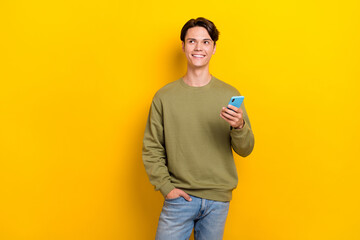 Photo of cheerful minded person hold telephone look empty space isolated on yellow color background