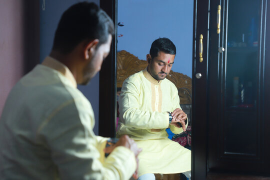 Hindu religious young handsome groom being ready by sitting in front of a mirror inside home 