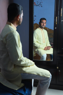 Hindu religious young handsome groom being ready by sitting in front of a mirror inside home 