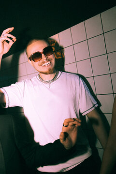 Smiling young man dancing against illuminated white wall