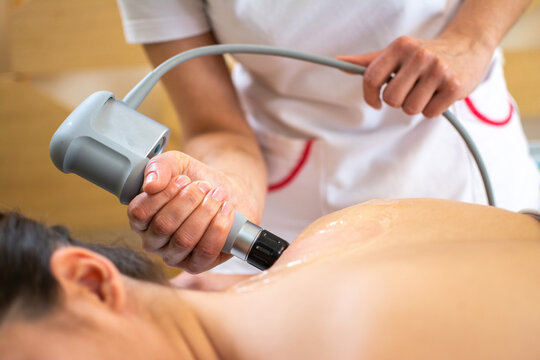 Close up of extracorporeal shockwave therapy in beauty salon. Physical therapy for neck and back muscles,spine with shock waves. Young woman wearing protective mask during treatment in salon.