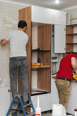 Two craftsmen, furniture makers and assemblers, are installing a modern kitchen in a home, tools in...
