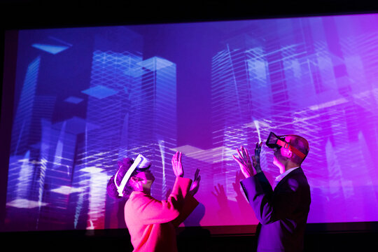 Business colleagues with futuristic glasses gesturing by projection screen at convention center