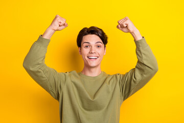 Portrait of delighted cheerful person beaming smile raise fists luck isolated on yellow color...