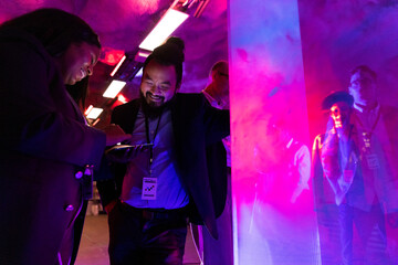 Smiling female entrepreneur sharing smart phone with male colleague at illuminated convention center