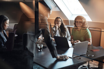 Female entrepreneurs discussing over laptop seen through glass during meeting in office