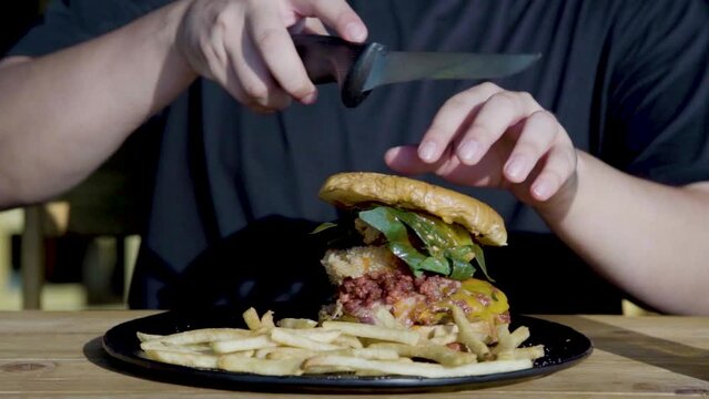 Primer plano de manos cortando una hamburguesa con papas a la francesa, lechuga y vegetales