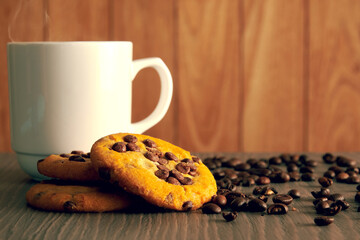 White coffee mug with the baked oatmeal cookies with chocolate and raw coffee grain. Breakfast snacks and drink. Copy space for text