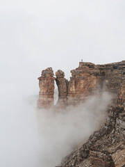 Vertical view of sharp rocks in the fog. Mountains in a dense fog. Mystical landscape with beautiful sharp rocks in low clouds.